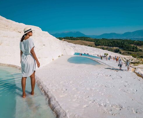 Woman in white dress standing in Pamukkale thermal pools with travertine terraces