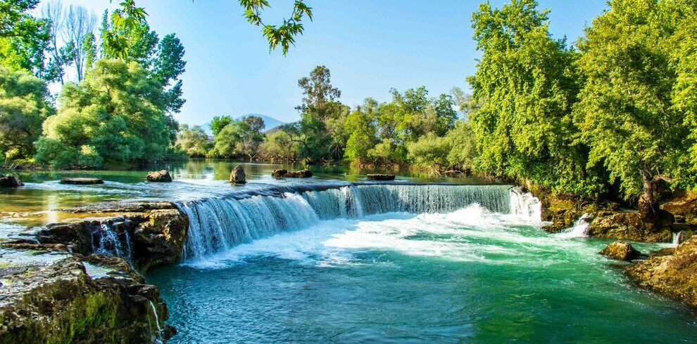 Manavgat Waterfall cascading over rocks into a serene river below.