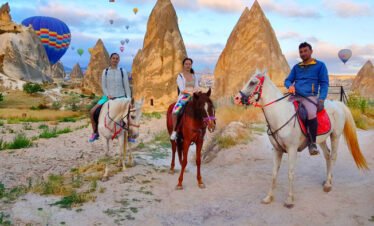 Daytime hot air balloon ride over Cappadocia, with horses grazing in the foreground
