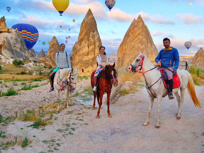 Daytime hot air balloon ride over Cappadocia, with horses grazing in the foreground