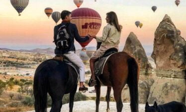 Couple enjoying a hot air balloon ride over Cappadocia's unique landscape, with horses in the foreground