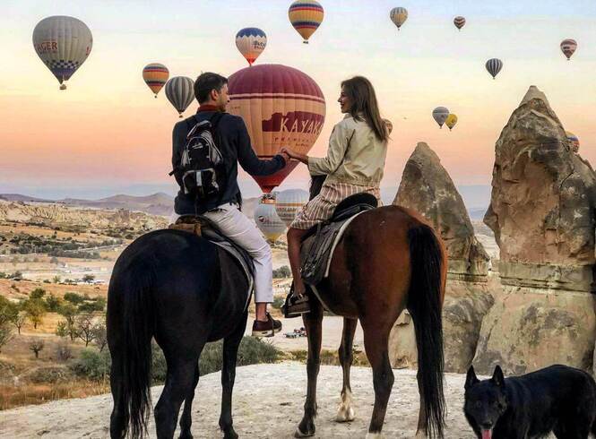 Couple enjoying a hot air balloon ride over Cappadocia's unique landscape, with horses in the foreground